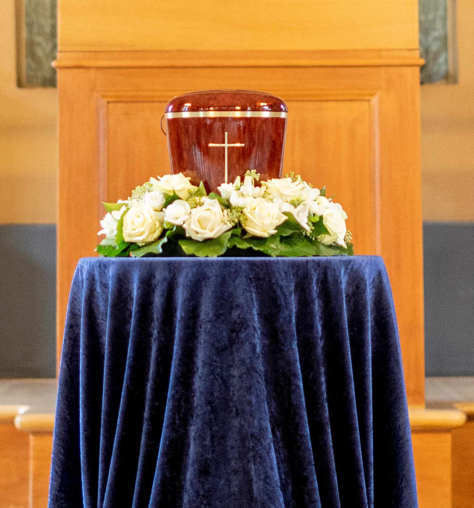 Eine Holzurne auf blauem Samt in der Trauerhalle, geschmückt von weissen Rosen